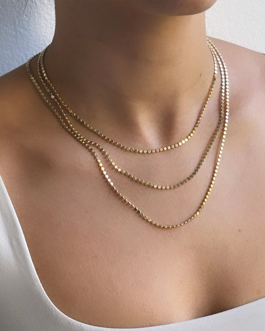 Model stacking three gold filled flat bead chain necklace close-up