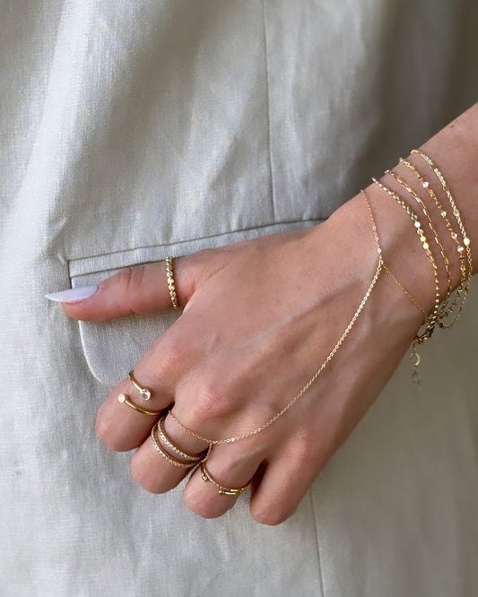 Model hand wearing gold ring stack, plain dainty hand chain, and thin bracelets