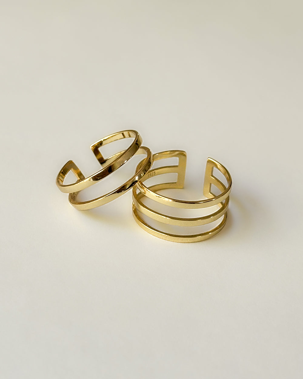Two adjustable rings- one with two gold parallel polished bands and one with three bands