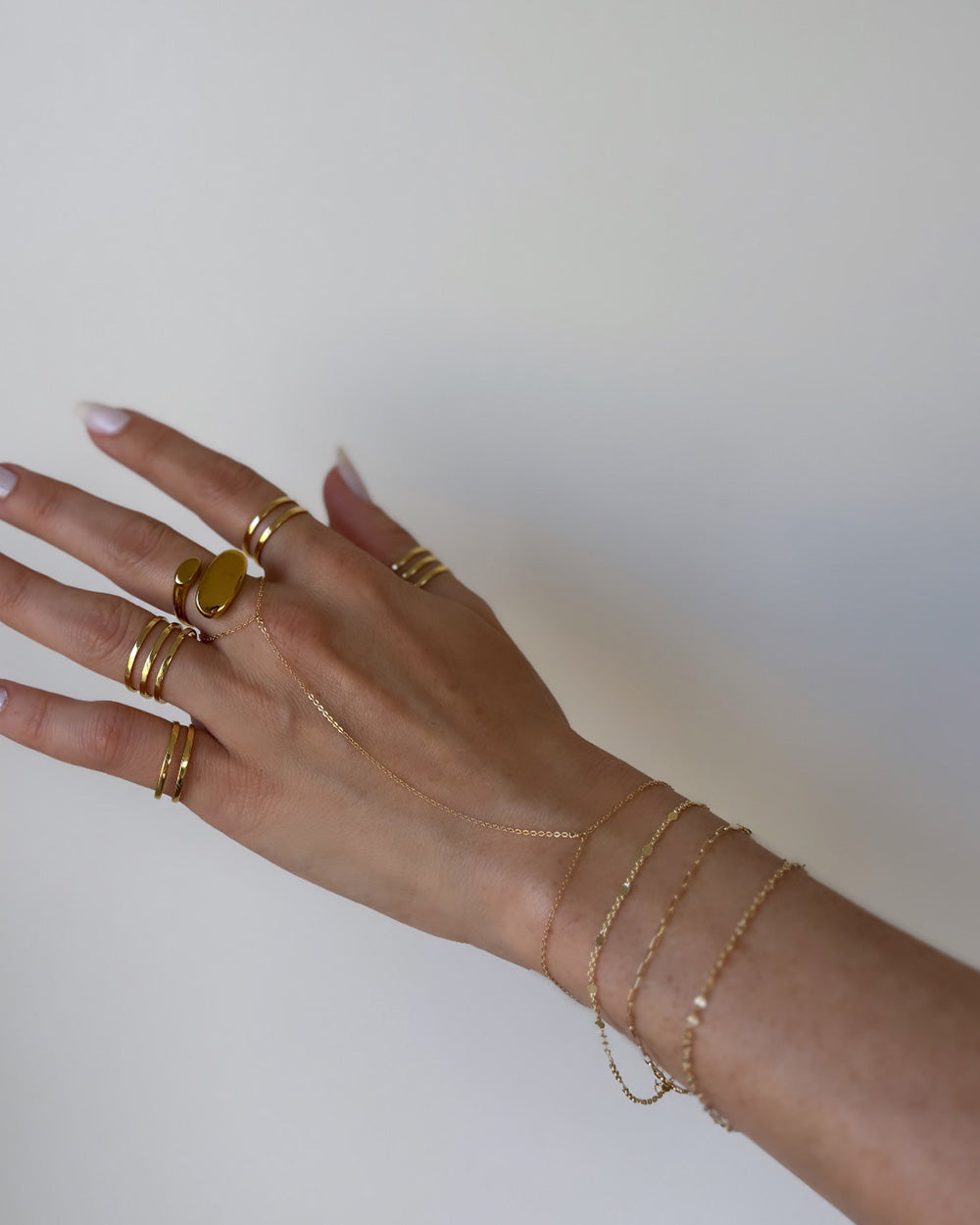 Model wearing thin gold plated dainty hand chain along with ring stack and bracelets