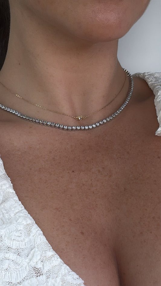 Close-up of round bezel CZ tennis necklace on model with another dainty choker