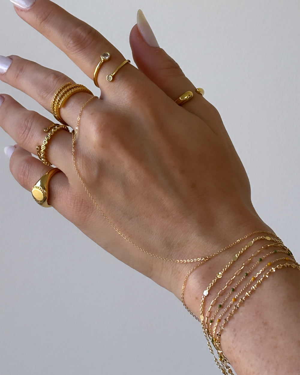 Model hand wearing gold ring stack, gold filled dainty hand chain and thin bracelets stack