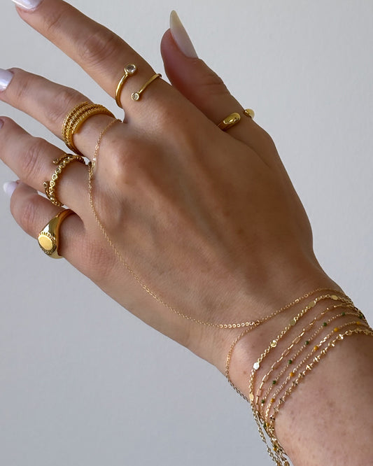 Model wearing mini dainty baby link chain bracelet stacked with other delicate Dumai bracelets, hand chain, and rings