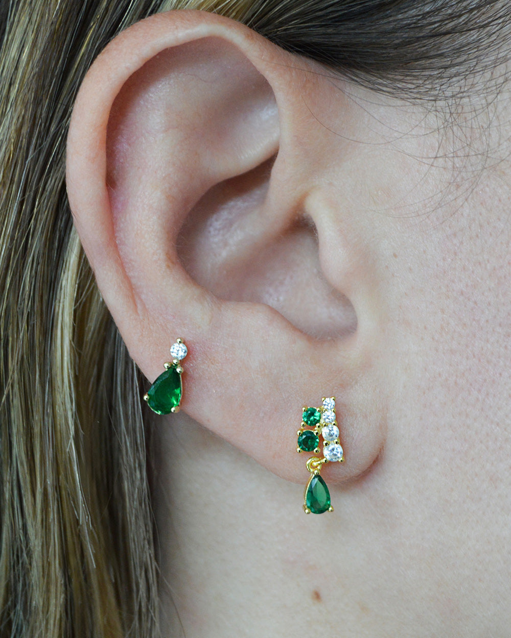 Model wearing gold-plated emerald teardrop studs and emerald and CZ studs