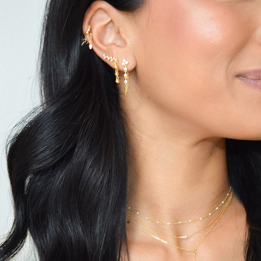 Model wearing chain Earrings with triangle top and dangling stones, paired with a tiny huggie, a dangling stud and a dangling climber earring