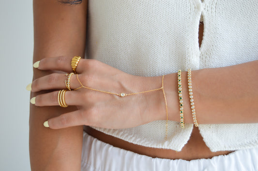 Sterling silver tennis bracelet with emerald and CZ stones on a model styled with dainty hand chain. Bold sculptural gold statement ring