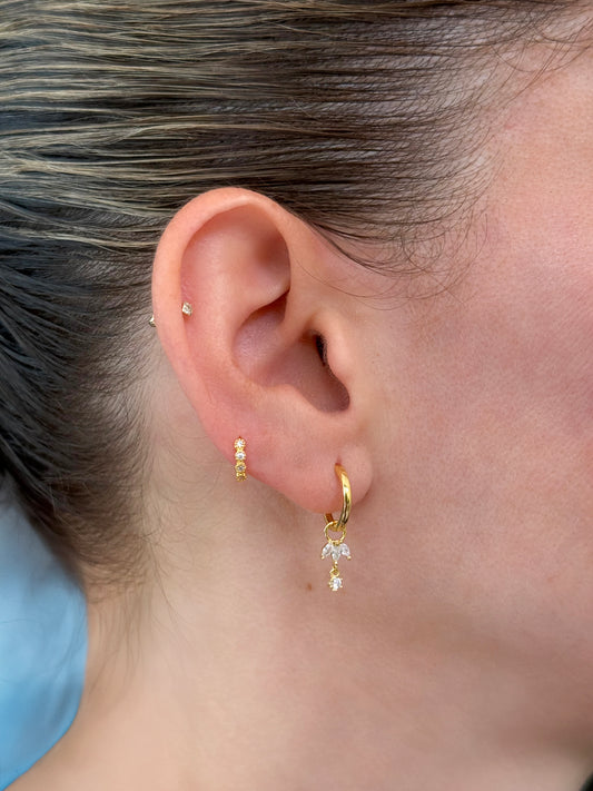 Dainty flower stone huggie earrings in 14K gold-coated sterling silver and tiny huggie with 3 CZ stones on model's ear