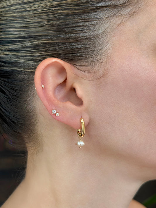 Model wearing 14K gold-coated sterling silver stud earrings featuring two small stones and a huggie with a dangling pearl detail