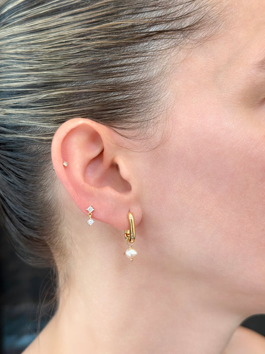Elongated 14k gold huggies with freshwater pearl charm on model styled with an additional CZ stud