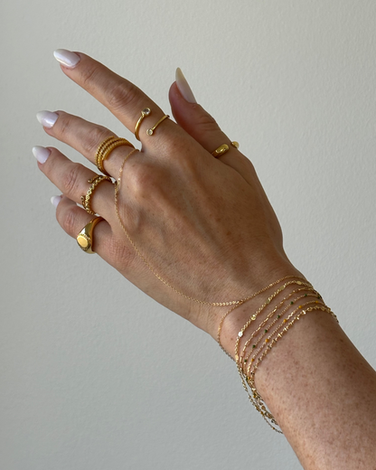Model hand wearing gold ring stack, plain gold filled dainty hand chain and thin bracelets